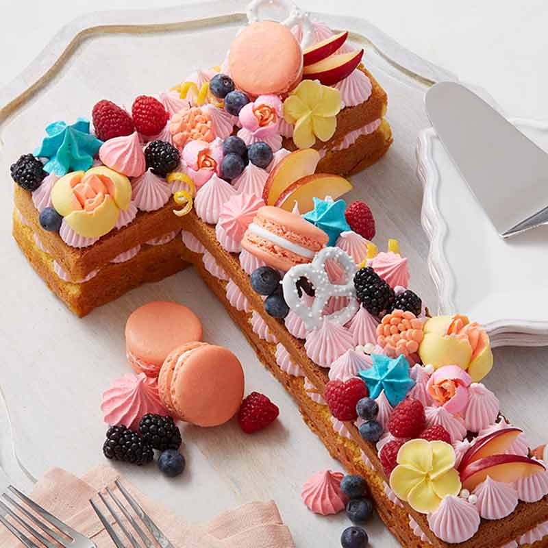 letter t cake pan decorated with multi color frosted, macarons and pretzels