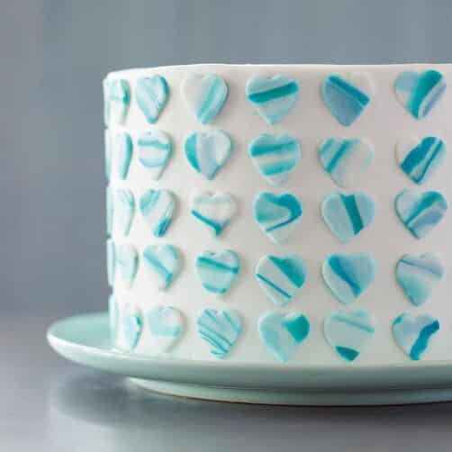 White cake with blue marbled fondant hearts lined in columns around the side.