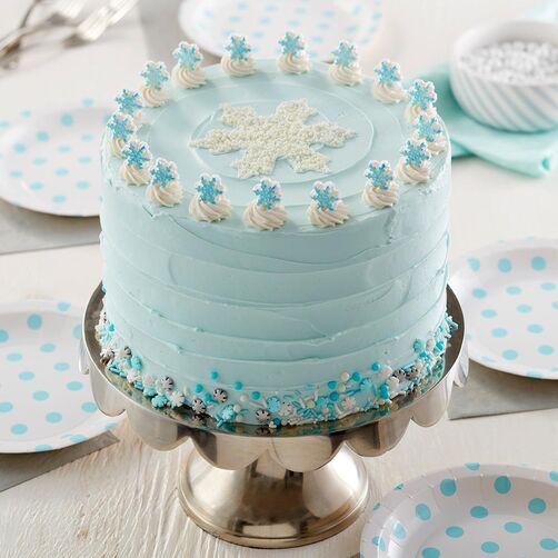 Light blue, round cake topped with little swirls around the border with small snowflake edible decorations on each swirl. In the center of the top is a white, sprinkle snowflake. Around the bottom of the cake, it's lined with blue and white sprinkles.