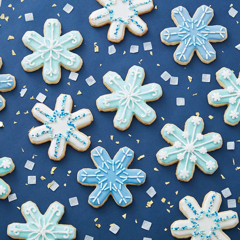 Snowflake sugar cookies decorated with white and blue cookie icing and white and blue sprinkles