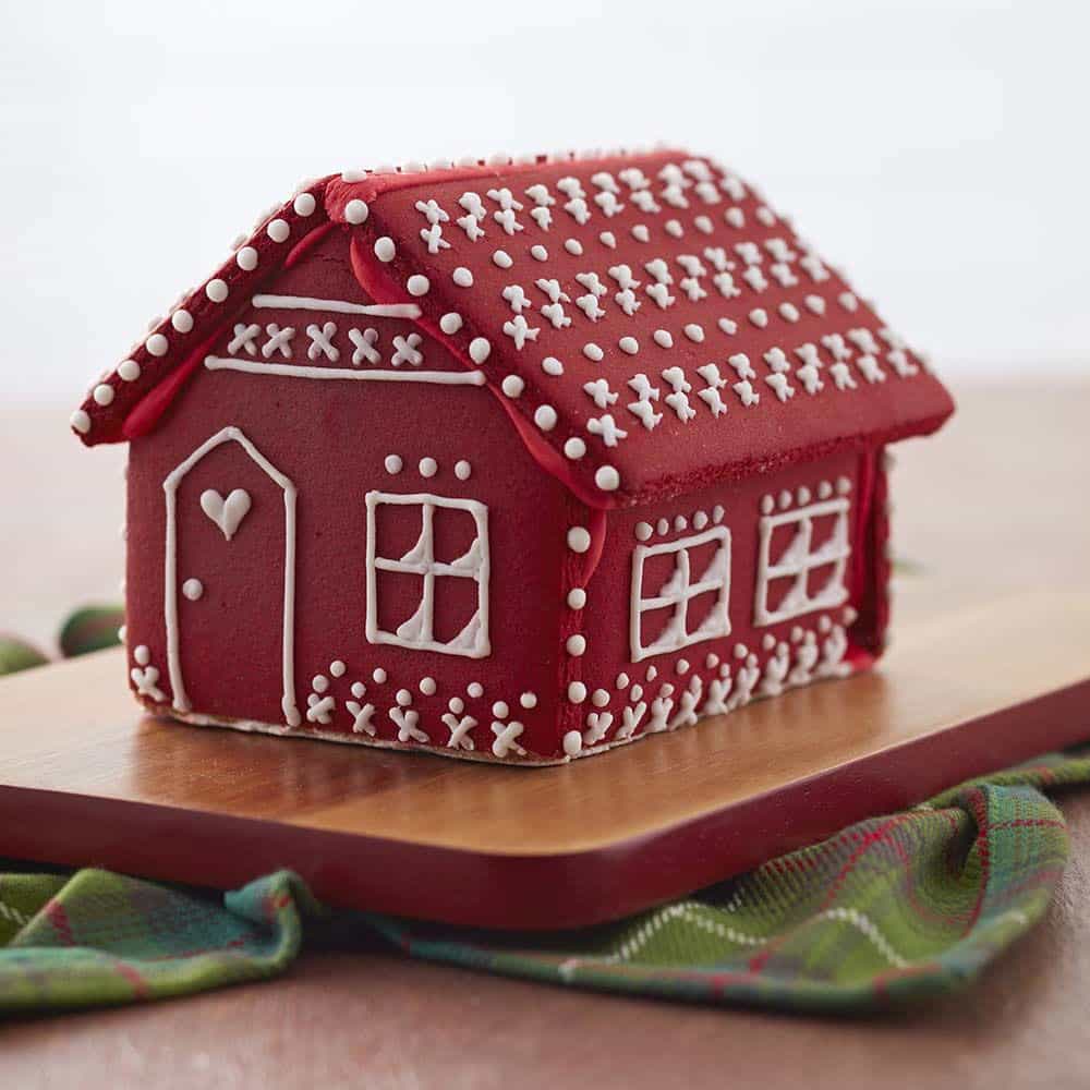 Christmas Red gingerbread house with white details on the roof and walls. Door has a little white heart with a window next to it.