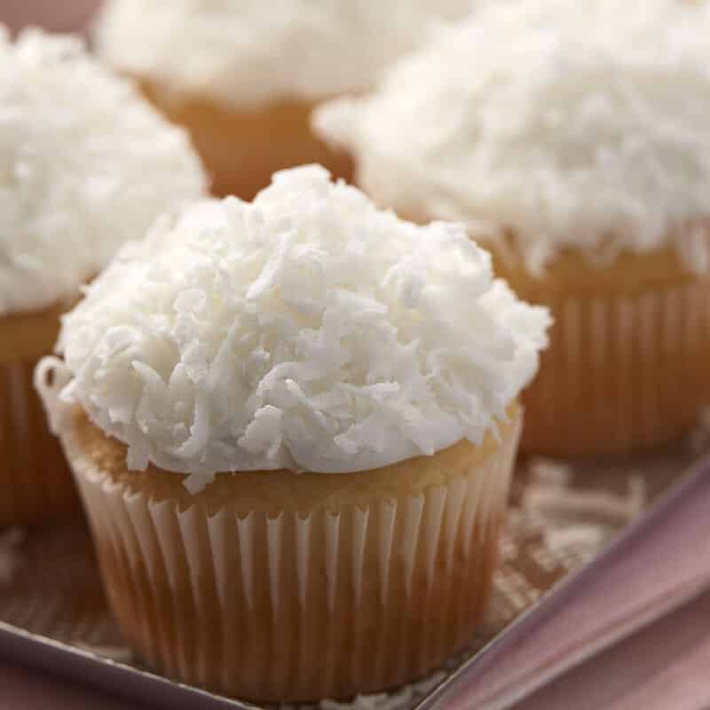 Almond cupcakes topped with frosting and coconut shavings