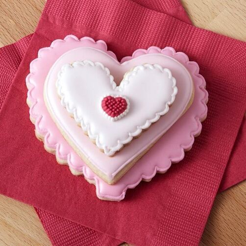 Stacked heart-shaped cookies in shades of pink and white with a heart-shaped icing decoration on top