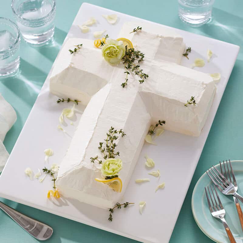 Herbs, carnations, and lemon top this white cross cake