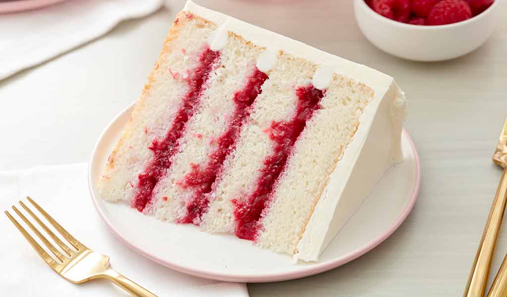 raspberry filled cake frosted with white buttercream frosting on a plate