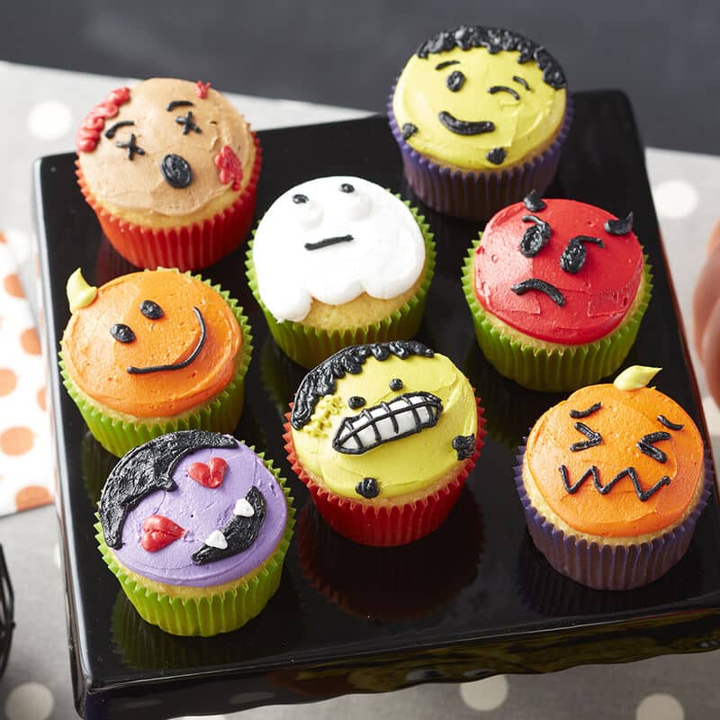 Cupcakes decorated like Halloween Emojis - Dracula with heart eyes, Frankenstein face, pumpkins, ghost, and red devil.