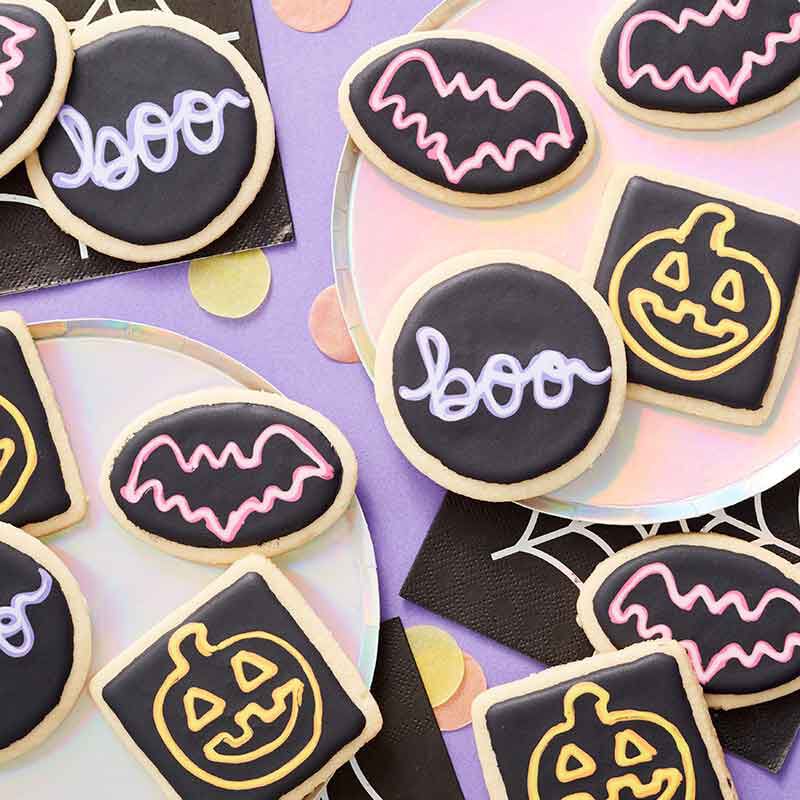 Shaped cookies decorated in black royal icing with pink bats, orange jack-o-lanterns, and "boo" drawn like neon signs