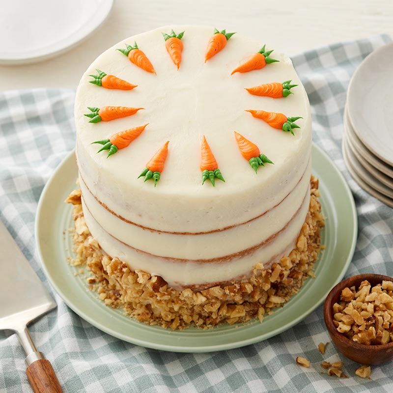 Round carrot cake with cream cheese frosting and walnuts. Topped with buttercream piped carrots